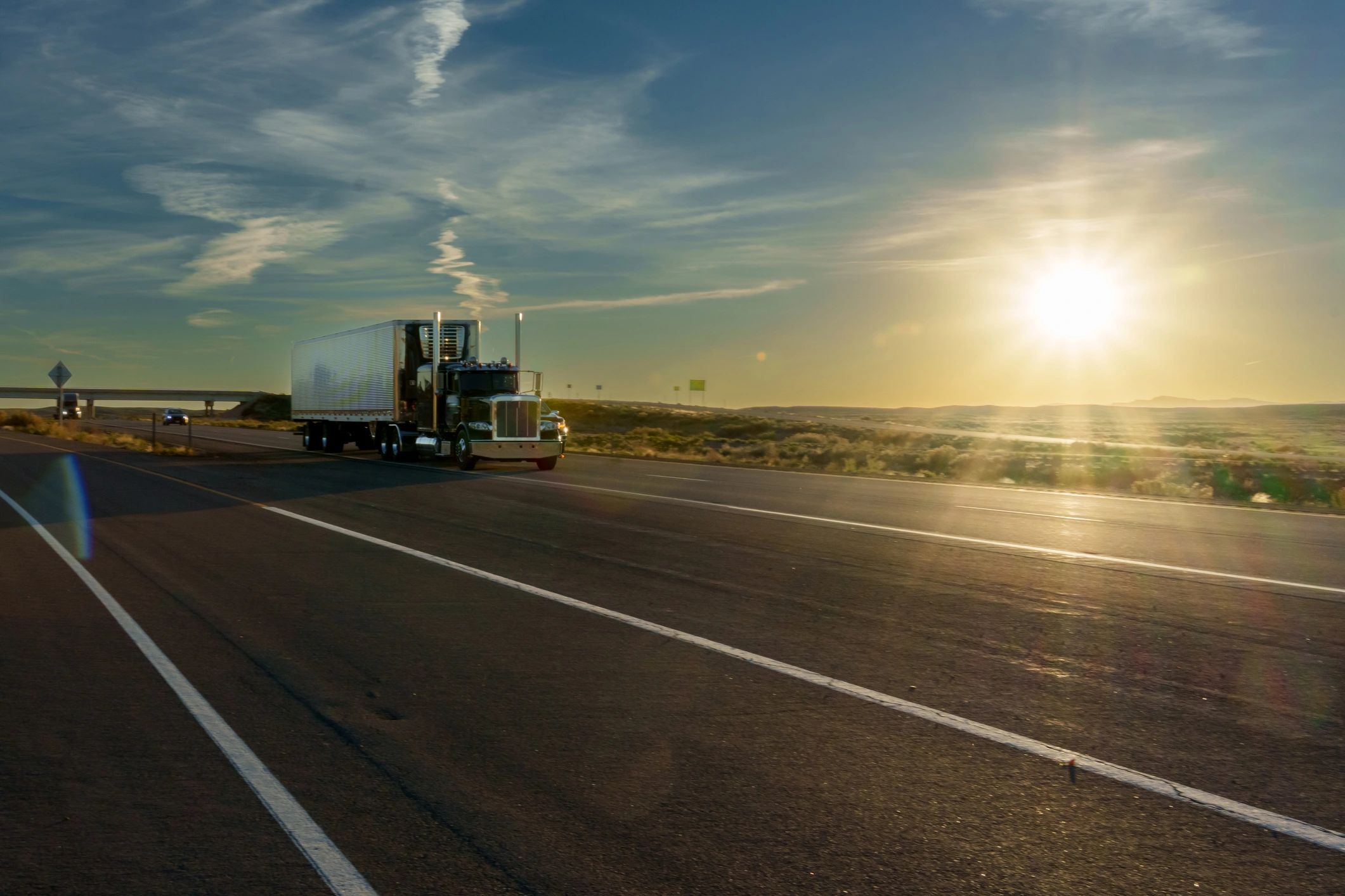 Semi-truck driving on highway at sunrise